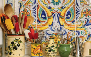 Cooking utensils displayed in patterned ceramic jars and vases against a colorful tiled backsplash.